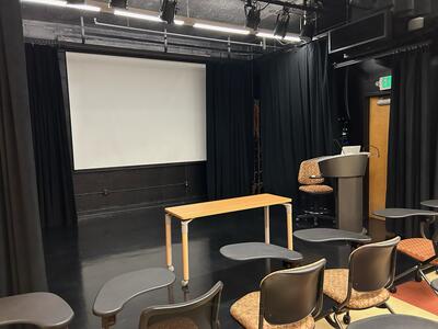 Second view of this space, closer up at front of lecture space featuring table and instructor lectern.